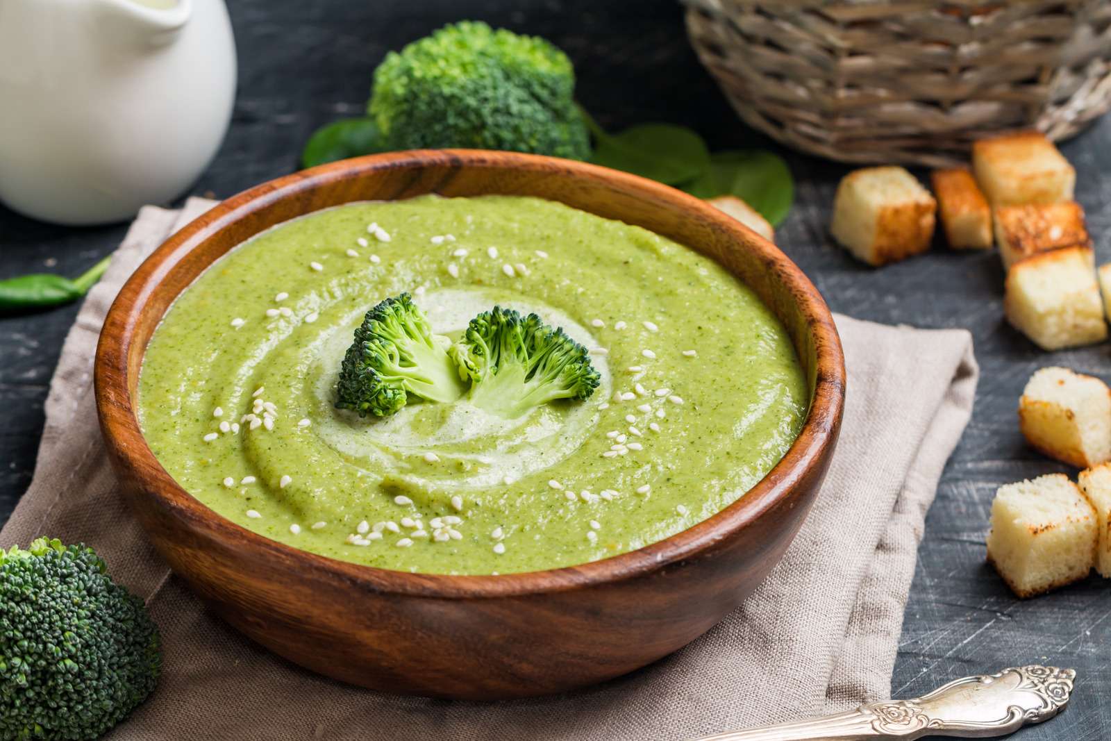 Wooden bowl of broccoli cream soup on black table