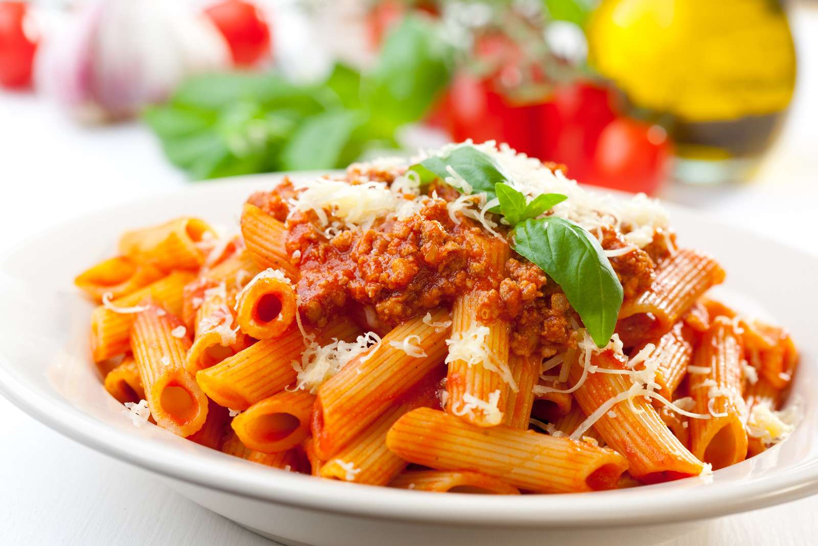 Plate of penne bolognese with ingredients in the background.