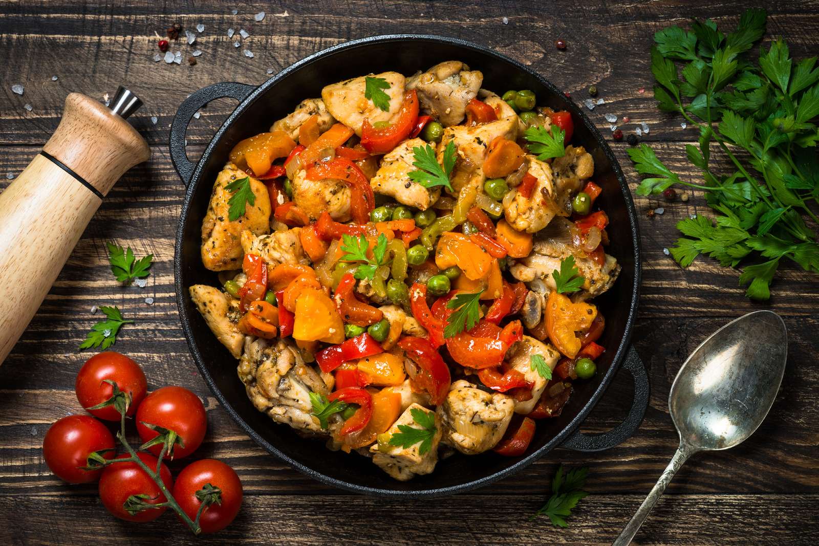 Chicken Stir fry with vegetables in the black iron plate. Top view on dark wooden background.